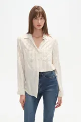 Camisa de viscosa color crema con finas rayas verticales negras, corte al cuerpo, cuello camisa y dos bolsillos frontales con tapa. Posee botones frontales y mangas largas con puño.