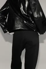 Jean de cinco bolsillos, tiro alto, color marrón oscuro o negro, con piernas anchas y rectas. Presenta cierre frontal con botón y remaches metálicos dorados.