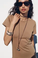 Vestido largo color marrón claro, de corte recto, con cuello redondo, mangas cortas y bajo asimétrico con volados.