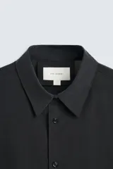 Camisa negra de corte relaxed fit confeccionada en tejido fluido con mezcla de viscosa. Tiene cuello solapa, manga larga con puño abotonado y cierre frontal con botones.