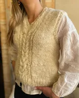 Chaleco de lana merino color crudo, tejido a mano con punto trenzado central y cuello en V.