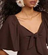 Vestido corto evasé color marrón chocolate, con escote corazón, nudo en el escote, mangas cortas con volados, lastex en la espalda y volado en el bajo.