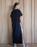 Vestido largo color crudo con cuello redondo y mangas cortas con ribete negro. Tiene corte recto y aberturas laterales en el ruedo.