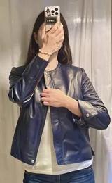 Chaqueta de cuero azul marino con corte entallado, cuello redondo, cierre frontal con cremallera oculta, mangas largas y bolsillos laterales ocultos.