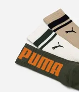 Kit de tres pares de medias deportivas Puma de caña larga. Un par color beige con dos rayas marrones horizontales en la parte superior y logo marrón en el tobillo. Un par color crema liso con logo blanco en el tobillo. Un par color marrón con una raya blanca horizontal en la parte superior y logo blanco en el tobillo.