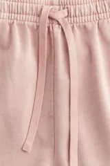 Short rosado de felpa de algodón, con cintura elástica ajustable con cordón, bolsillos laterales y traseros, y aberturas laterales en el ruedo.