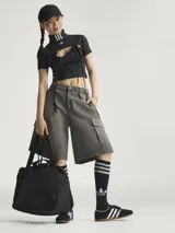 Crop top negro de Adidas con cuello alto, mangas cortas y aberturas frontales con lazos. Presenta las tres líneas características de la marca en color blanco en el cuello y el logo en el pecho.