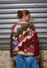 Sweater de lana color crema con cuello redondo, mangas largas y diseño tejido con motivos geométricos y florales en tonos marrones, rojos, verdes, azules y rosas.