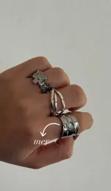 Set de tres anillos plateados: uno con flores, otro doble y otro ancho con una piedra blanca incrustada.