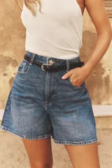 Shorts de denim blanco, tiro alto, estilo mom fit, con cinco bolsillos y cierre frontal con cremallera y botón.