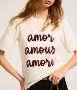 Remera color crema de algodón, corte slim, con cuello redondo y mangas cortas. Estampa frontal con las palabras 'amor', 'amour' y 'amore' en color borgoña.