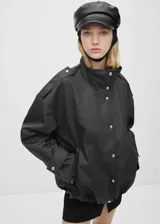 Anorak negro oversize con cuello alto, cierre frontal con botones y cremallera oculta, mangas largas con puños abotonados y bolsillos laterales con cremallera.