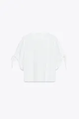 Camiseta blanca de algodón con cuello redondo, corte recto y mangas cortas ajustables con lazadas.