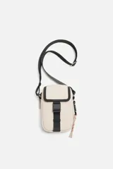 Bandolera vertical color beige con detalles en negro. Tiene un compartimento principal con cremallera, un bolsillo interior plano y un bolsillo frontal con hebilla de liberación rápida. El asa de hombro es ajustable y extraíble.