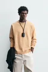 Sweater color arena con textura jaspeada, de corte recto, cuello redondo y mangas largas con terminaciones acanaladas.