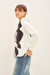 Blazer con estampado abstracto en tonos beige, negro y blanco. Tiene solapas blancas y está adornado con tachas termofijadas en el frente. Se cierra con un cinturón negro con una flor grande.