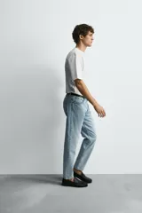 Jeans de denim de algodón, color negro lavado, con tiro medio, corte ajustado en cadera y muslos, y pierna que se estrecha hacia el tobillo. Presenta cinco bolsillos y cierre frontal con cremallera y botón.