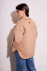 Sobrecamisa negra de gamuza vegana con calce oversize, cuello camisero, cierre con botones a presión, mangas largas con puños abotonados y bolsillos de parche en el pecho.