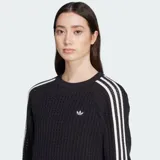 Buzo de crochet negro con calce amplio, cuello redondo acanalado y las icónicas tres franjas blancas de Adidas en las mangas. Presenta el logo del trébol de Adidas bordado en el pecho.