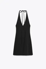 Vestido corto negro con cuello halter y lazada. Tiene bolsillos laterales ocultos y forro interior combinado. El cierre es en la espalda con cremallera oculta.