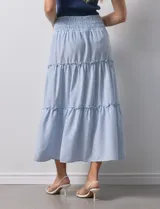 Falda midi a rayas verticales celestes y blancas, con pretina ancha elastizada en punto smock y volados en los cortes.