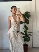 Vestido largo de encaje color nude, con escote halter y espalda descubierta. Incluye cinturón blanco con apliques metálicos.