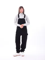 Mono enterizo negro de corte holgado con tirantes regulables y bolsillos laterales. Presenta un bolsillo tipo parche en el frente.