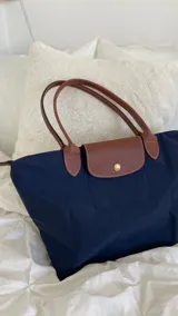 Bolso tote azul marino de nylon con detalles de cuero marrón en las asas y la solapa de cierre.