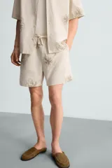 Bermuda regular fit color beige con bordados de flores en tono marrón. Tiene cintura elástica ajustable con cordón, bolsillos laterales y un bolsillo trasero de plastrón.