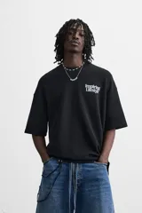 Sudadera negra de corte holgado con cuello redondo y mangas cortas. Estampa frontal y trasera con gráficos y textos en color blanco.