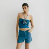 Top tipo bandeau color azul vibrante, ajustado al cuerpo, con tiras finas que se anudan al cuello (halter). Presenta una flor grande de tela de lino azul oscuro con detalles de mostacillas en el centro del escote.