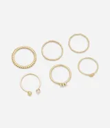 Set de seis anillos dorados de metal reciclado con diferentes diseños: texturizado, liso, con tres perlas pequeñas, con una perla y una esfera, y con una placa circular.