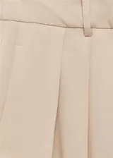 Pantalón color beige de corte wide leg, tiro medio, con trabillas, cierre frontal con botón, gancho y cremallera, detalle de pinzas y diseño largo.