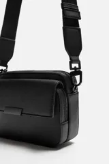 Bandolera negra con textura grabada, compartimento principal con cierre de cremallera, bolsillo interior con cremallera, bolsillo frontal con solapa y cremallera, asa de hombro removible y ajustable.