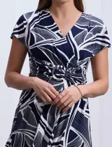 Vestido midi de seda fría con estampado abstracto en blanco y azul marino, escote en V cruzado, mangas cortas y cintura con hebilla decorativa.