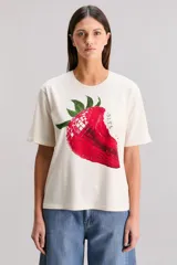 Remera color crudo de calce oversize, confeccionada en tejido jersey 100% algodón. Tiene cuello redondo, manga corta y estampa de una frutilla mordida.