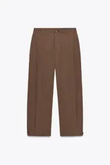 Pantalón marrón de tiro medio con trabillas en la cintura, bolsillos laterales, pinzas delanteras y bajo ajustable con trabilla y botón.