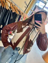 Campera de cuero color marrón rojizo (whisky) con detalles de piel de vaca (marrón y blanco) en el cuello y solapas. Se observa que está abierta, revelando un sweater de punto color crema con botones dorados debajo.