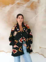 Saco de lana marrón con diseño geométrico multicolor, cuello con solapa, cierre frontal con botones y bolsillos delanteros.