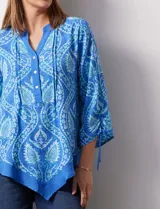 Blusa de gasa estampada marca Ruby Rd, de color azul. Tiene cuello a la base, escote en V y abertura central con botones. La delantera es plisada. Las mangas son ¾ con frunce. El ruedo y la espalda son asimétricos.