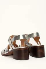 Sandalias plateadas de cuero con tiras entrecruzadas y hebilla lateral. Taco de madera de 6 cm.