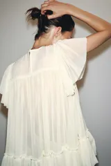 Top color crema de cuello redondo y manga corta, con detalle de bordado en el pecho y bajo con volantes. Cierre en la espalda con abertura y botón.
