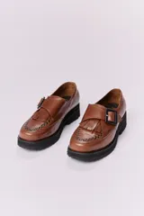 Zapato mocasín color marrón de cuero con hebilla metálica negra y detalle de flecos.