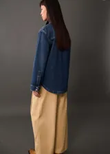 Camisa de jean azul con bolsillos de solapa en el pecho, manga larga con puños abotonados, diseño recto y oversize, cuello camisero y cierre delantero con botones.