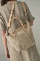 Cartera tipo tote de lana color beige con forro, cierre y asa de cuero regulable.