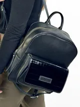 Mochila grande de cuero negro con bolsillo frontal de charol y cierre superior.