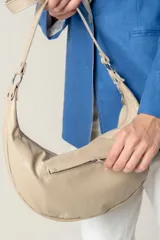 Cartera tipo bandolera de cuero sintético color celeste, con forma de media luna y tachas metálicas redondas plateadas en el frente. Posee correa ajustable y placa metálica con logo en la parte superior.