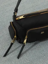 Bandolera negra de cuero vacuno con correa fina ajustable. Tiene cierre superior y forro interior de tejido jacquard. Incluye bolsillos frontales y laterales con cierre dorado y logo de la marca en dorado.