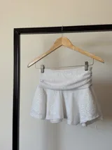 Minifalda blanca con lentejuelas, cintura alta fruncida y corte acampanado.