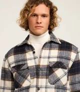 Campera trucker masculina de franela a cuadros en tonos blanco, negro y gris, con cuello inglés, abotonado delantero, bolsillos con solapa en el pecho y bolsillos laterales. Interior forrado en sherpa.